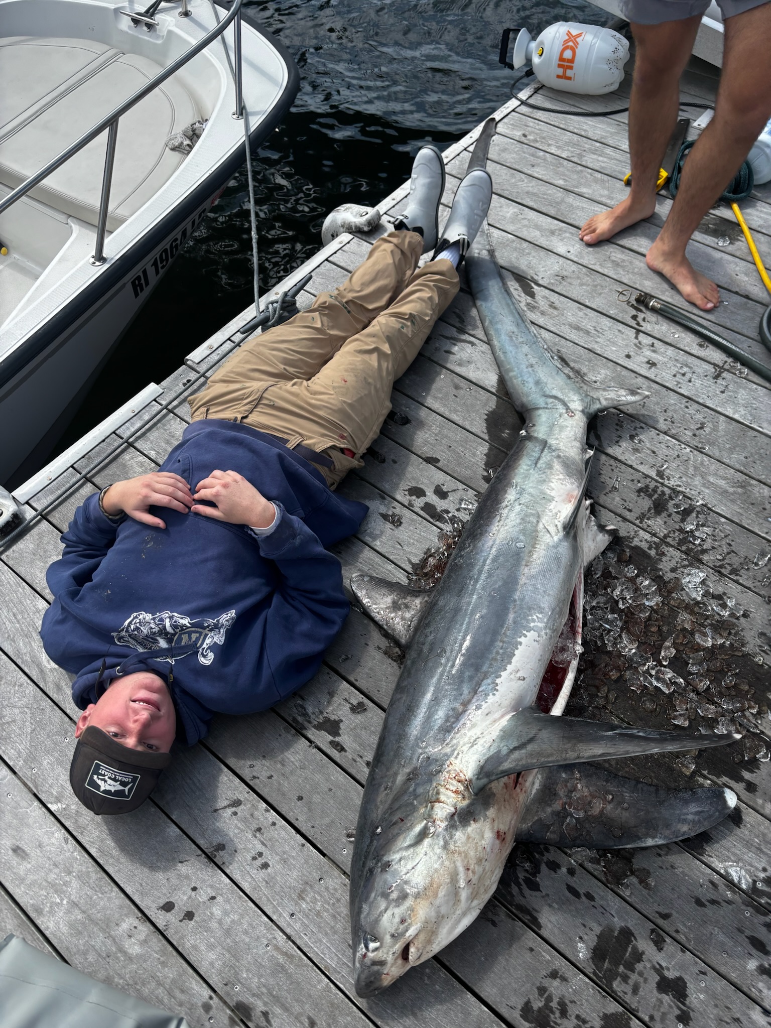 Person lying next to large mako shark on dock