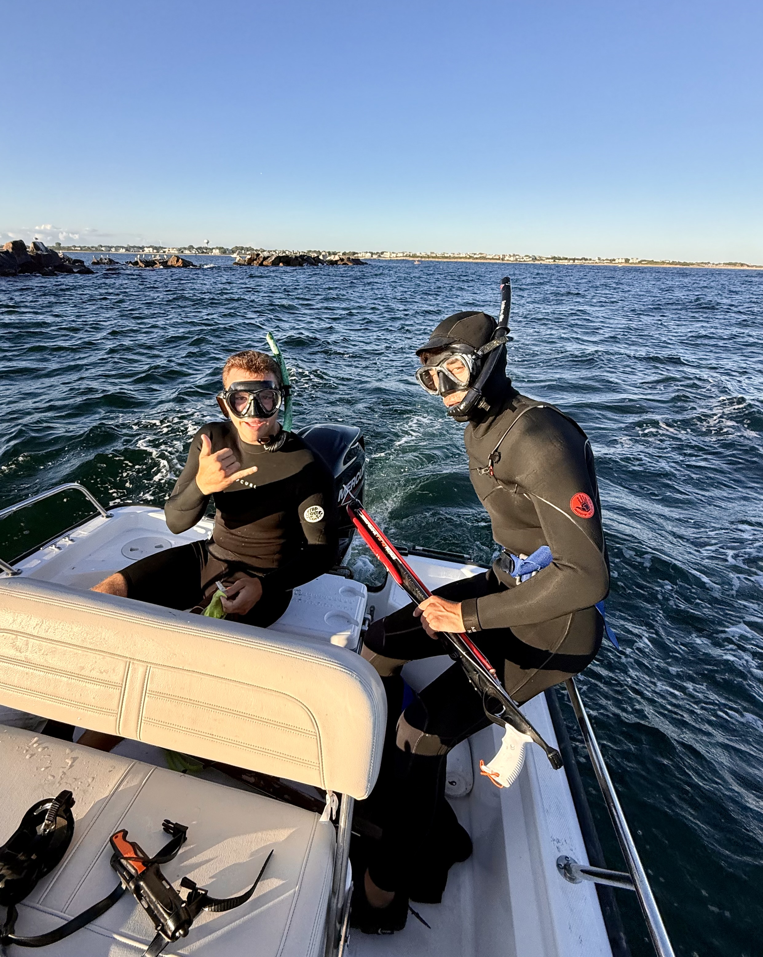 Two divers in wetsuits with spearguns on boat